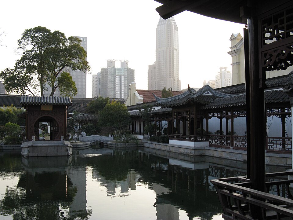煦园水景，池塘与亭台楼阁，远处可见现代城市天际线