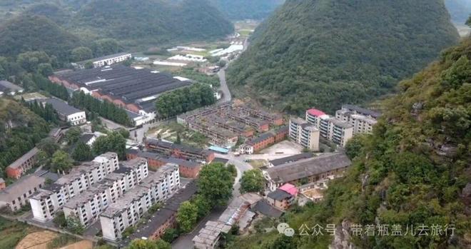 厂房散布在碾子山丘陵之间的景象，灰白色的车间建筑零散嵌在山谷树林中
