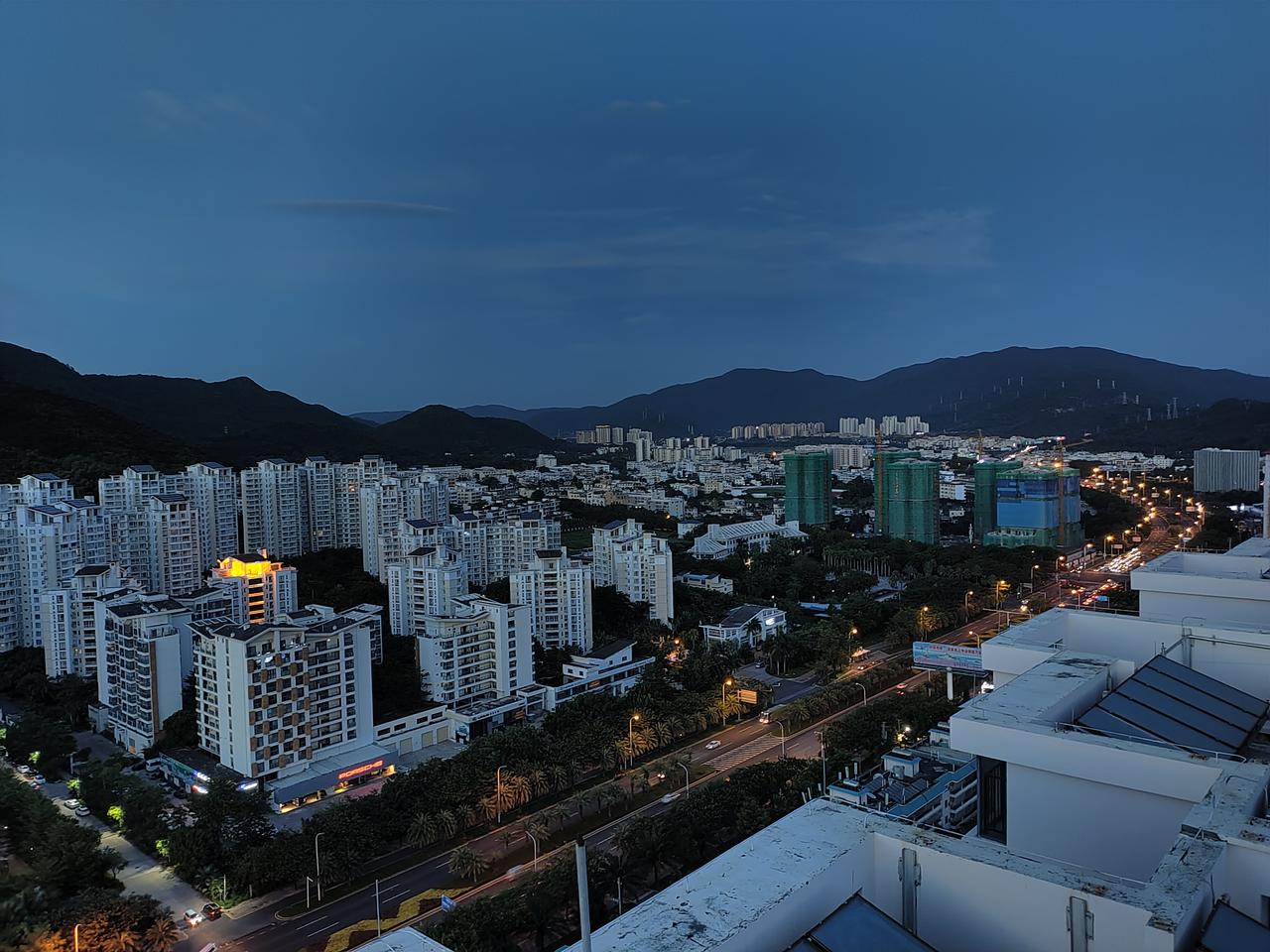 三亚迎宾路夜景，高层住宅和商业楼宇灯火通明，连接军港后勤区与旅游区的主干道车流稀疏