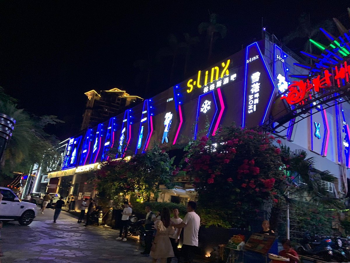 大东海酒吧街夜生活场景，S-LINX 林格斯酒吧霓虹灯点亮，热带绿植环绕，游客在石板路上漫步