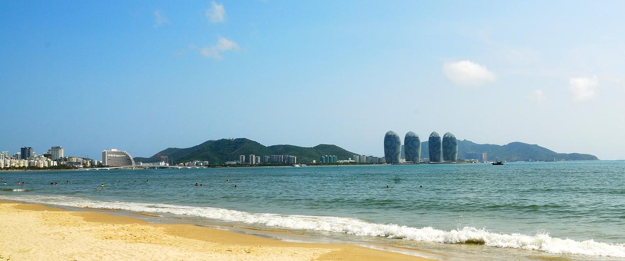 从三亚湾海滩远眺凤凰岛:五栋蛋形超高层建筑浮在海面上,背后是三亚城市天际线和山峦