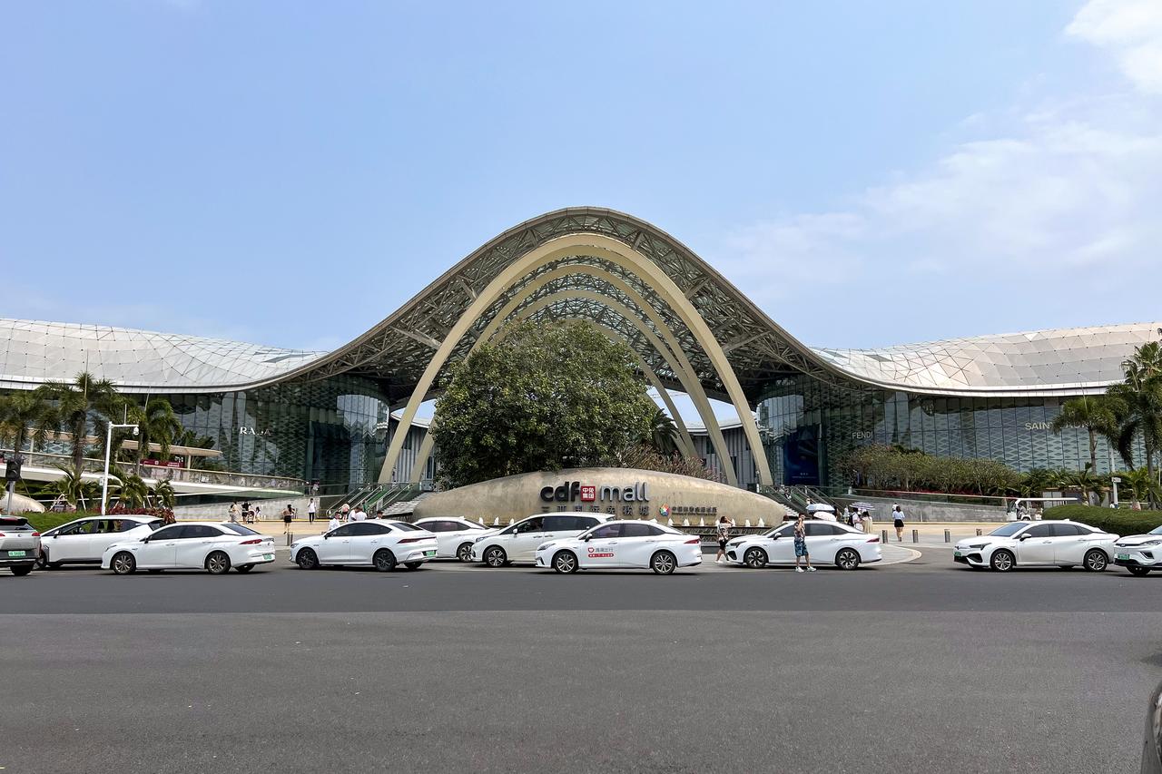 三亚国际免税城建筑外观，曲线玻璃幕墙和白色钢结构屋顶形似一朵盛开的海棠花，入口广场宽阔