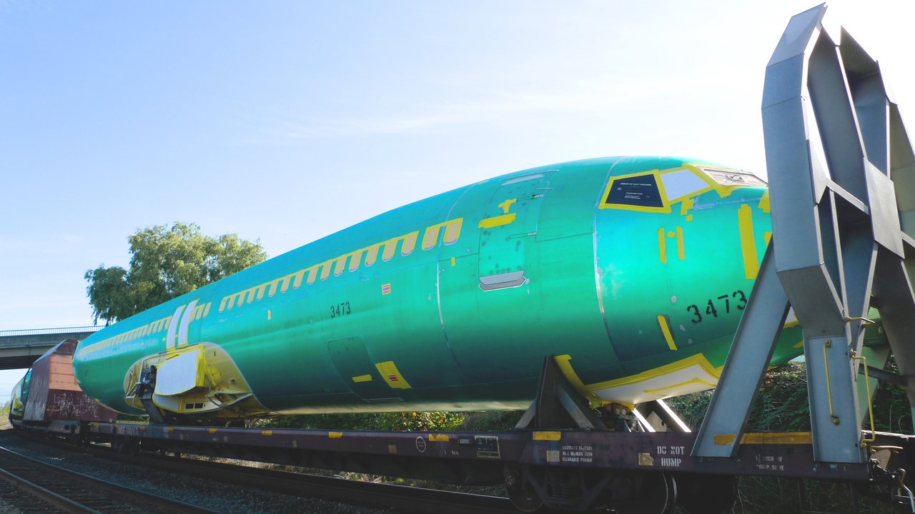 BNSF 铁路平板车上的 737 机身列车，覆绿色保护胶膜