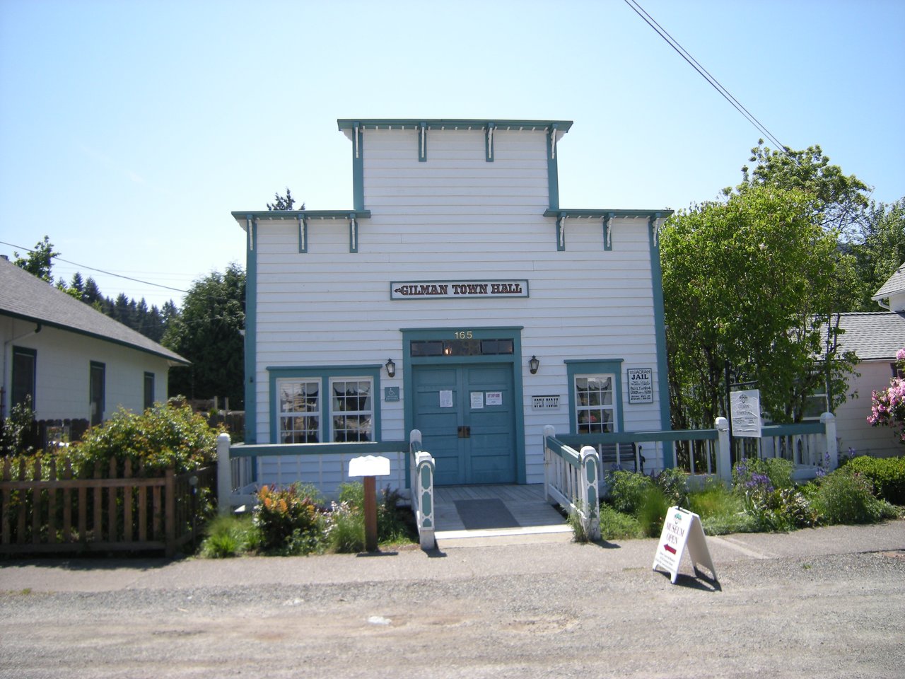Gilman Town Hall Museum 的 north 立面，白色 7 英寸 lapped 板、阶梯式 false-front 山墙、双扇木门、十支锯花托架