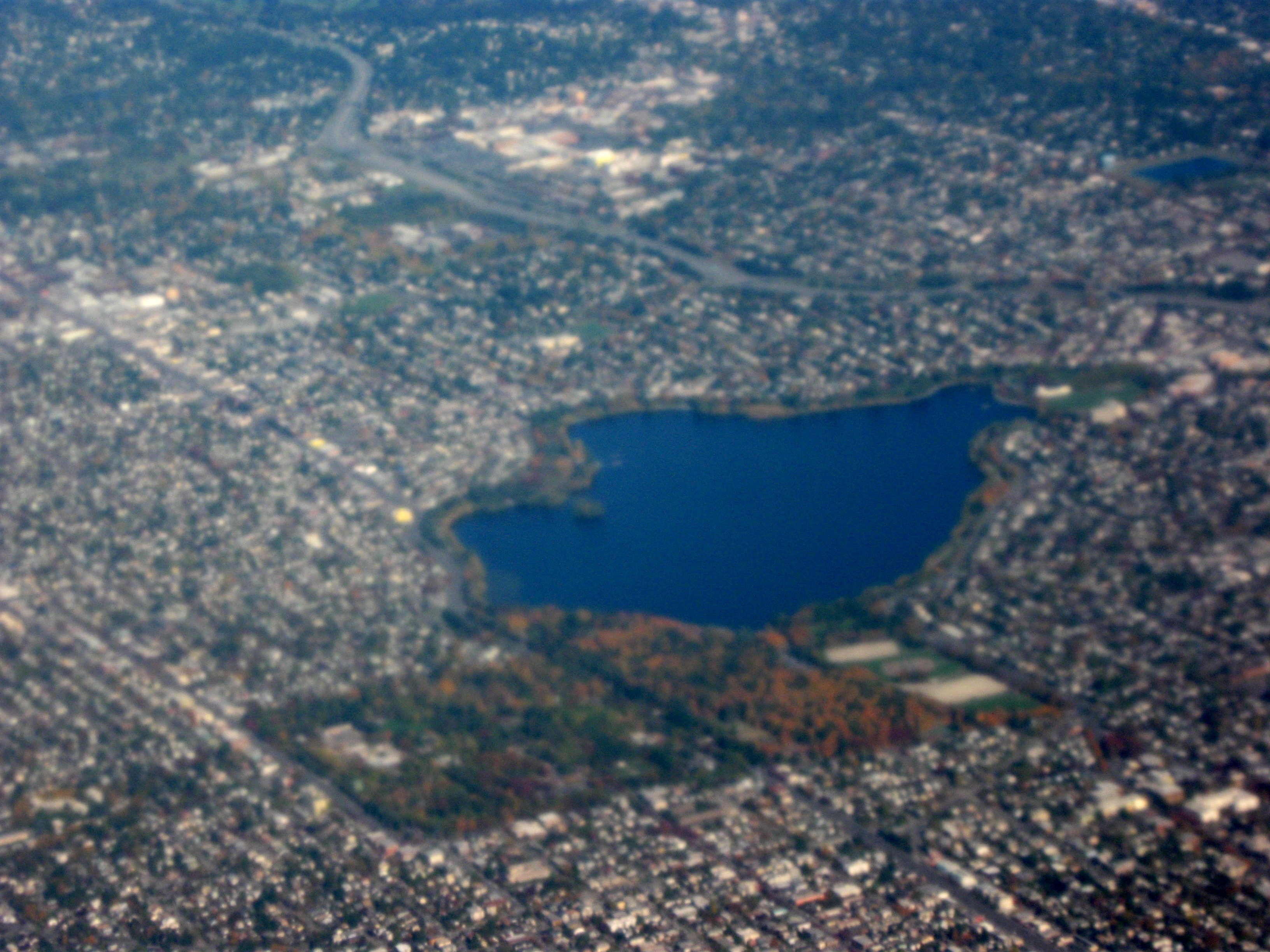 从空中向东北看 Green Lake 与周围密集街区，湖体居中，南端 Aurora Avenue/I-5 高速从后方穿过