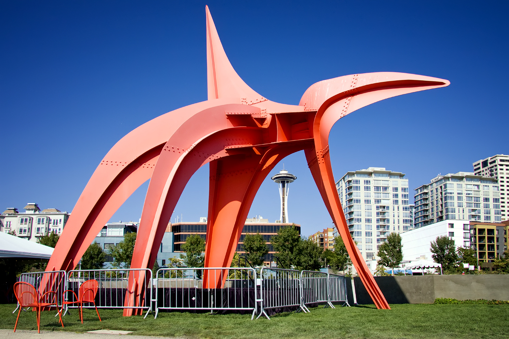 Calder Eagle（1971）红色 stabile 立在 OSP 跨 Elliott Avenue 步行桥的水侧端点，背后是 Elliott Bay 与 Olympic Mountains 的天际线