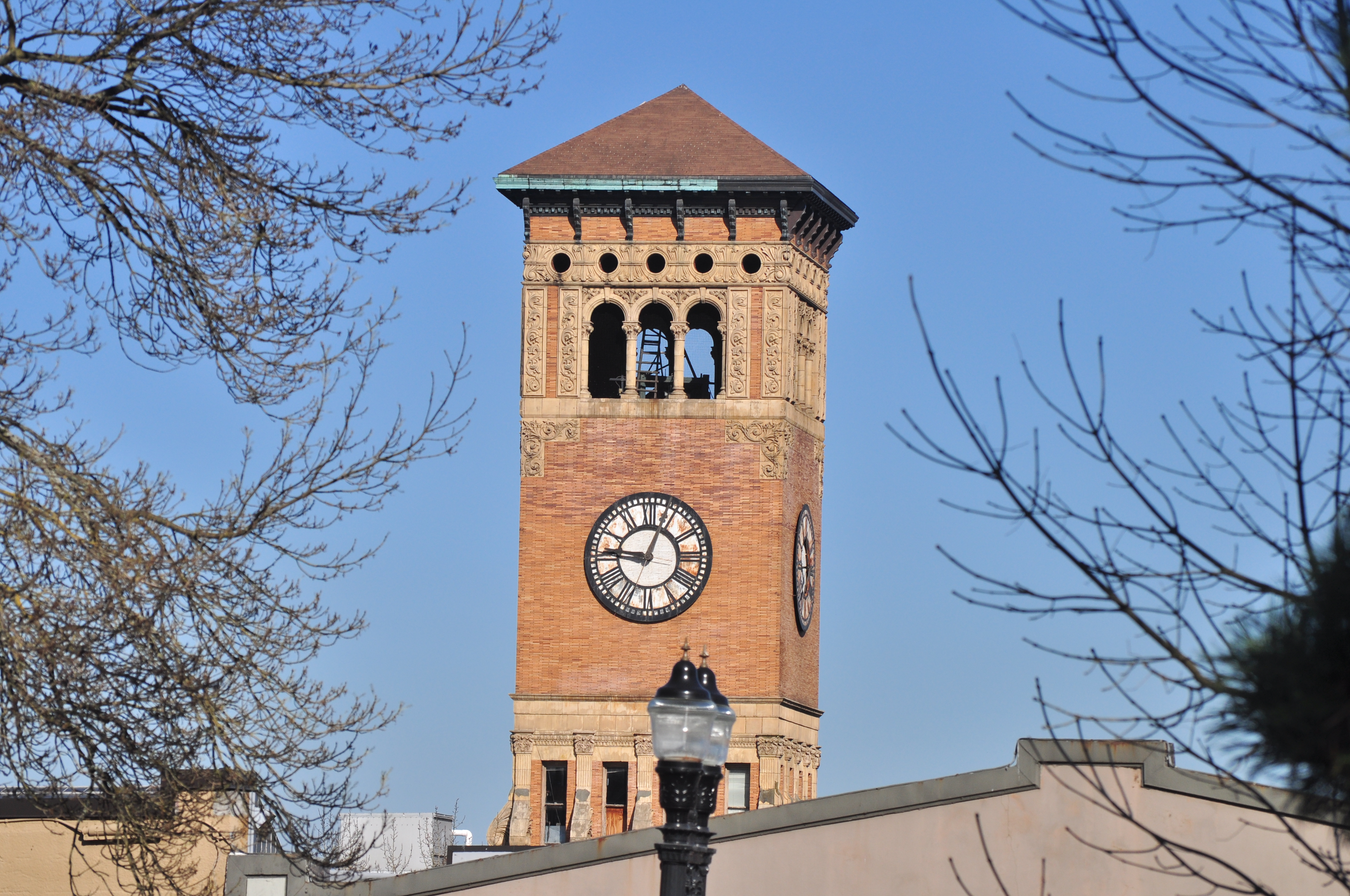 Tacoma Old City Hall 钟塔顶部细节，三组拱窗、上方一圈圆窗与陶土饰带、铜瓦尖顶轮廓