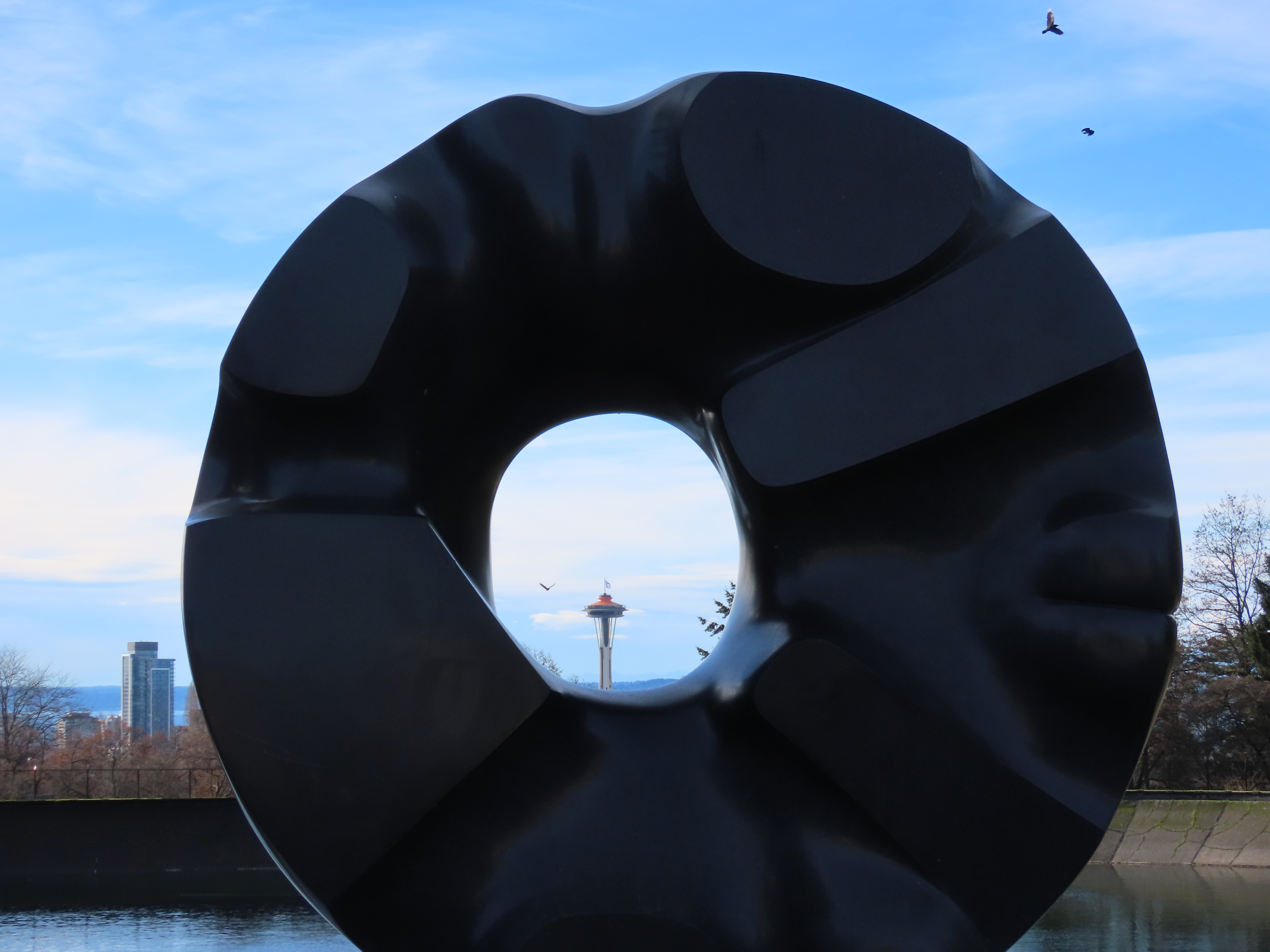 Black Sun 雕塑透出的镂空对准远处 Space Needle 的塔尖