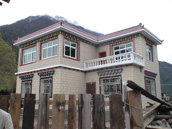 一栋新建藏式民居近景,可见藏式彩绘窗框与砖混结构墙体的结合