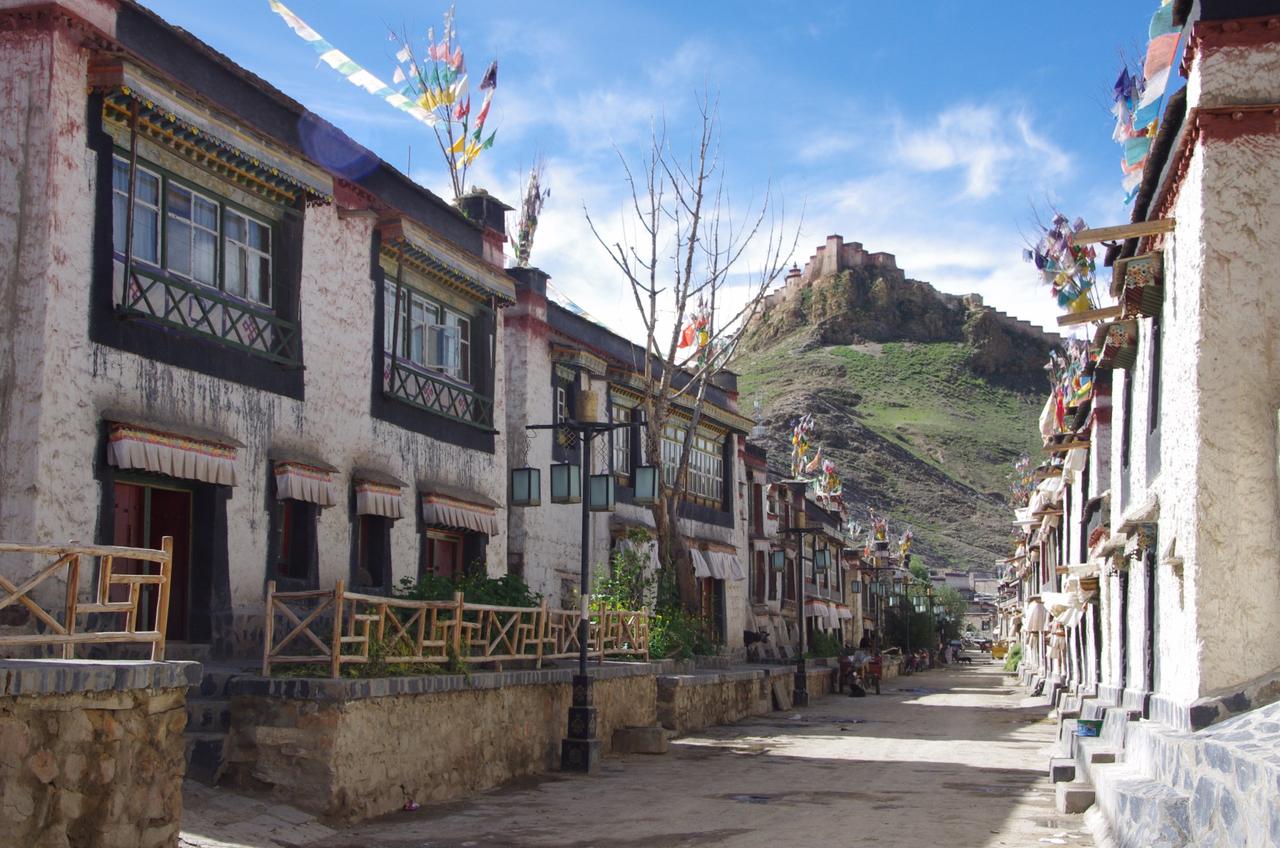 江孜古城藏式碉房街巷,屋顶可见五色塔觉经幡,背景为宗山古堡