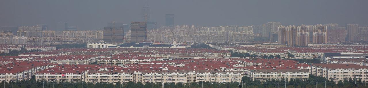 站在古城向东远眺，传统灰色屋顶线在前景铺开，工业园区高层建筑群在 5 公里外升起，天际线形成一道清晰的制度分界