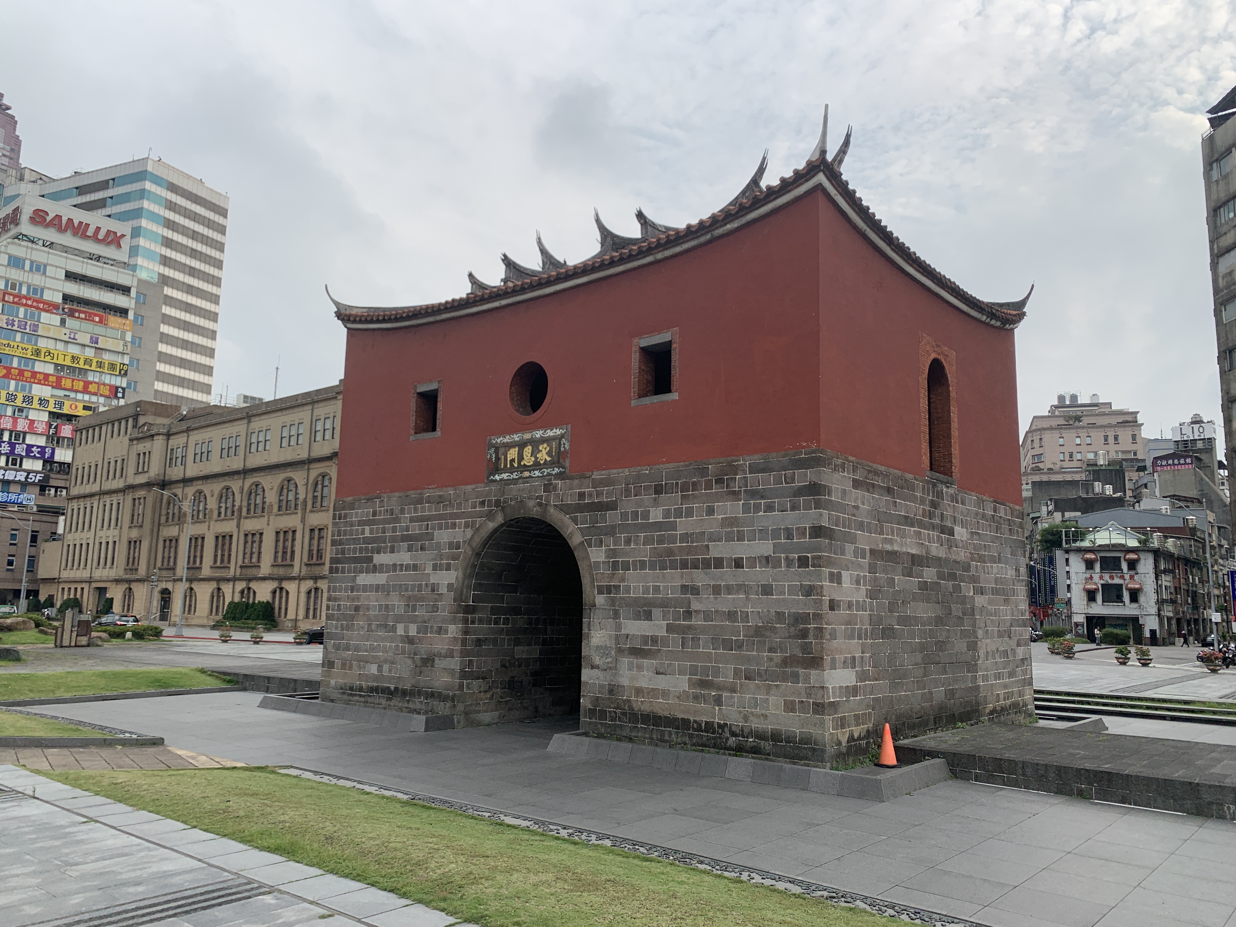 A historic red brick and stone gate with traditional roof ornaments stands amids