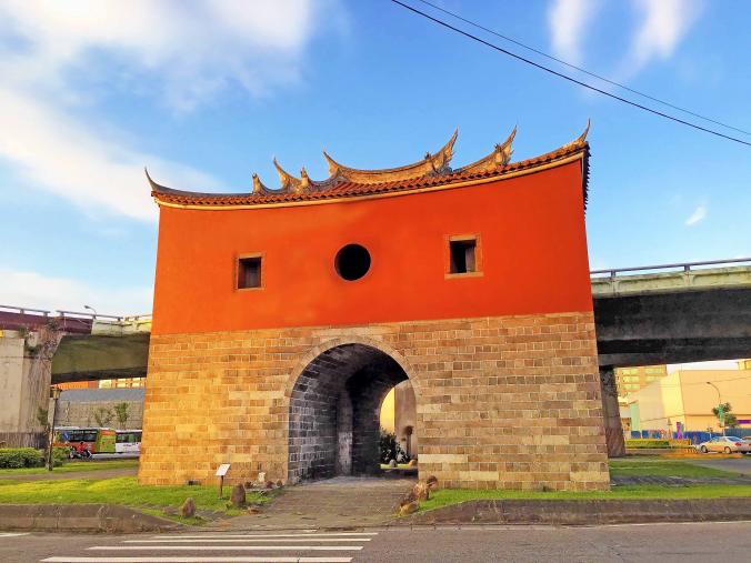 A traditional Taiwanese gate with a red upper structure and a stone brick founda