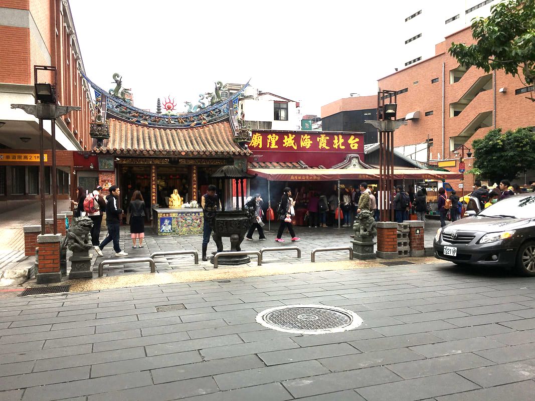 A group of people gather outside a traditional Chinese temple with ornate roof d