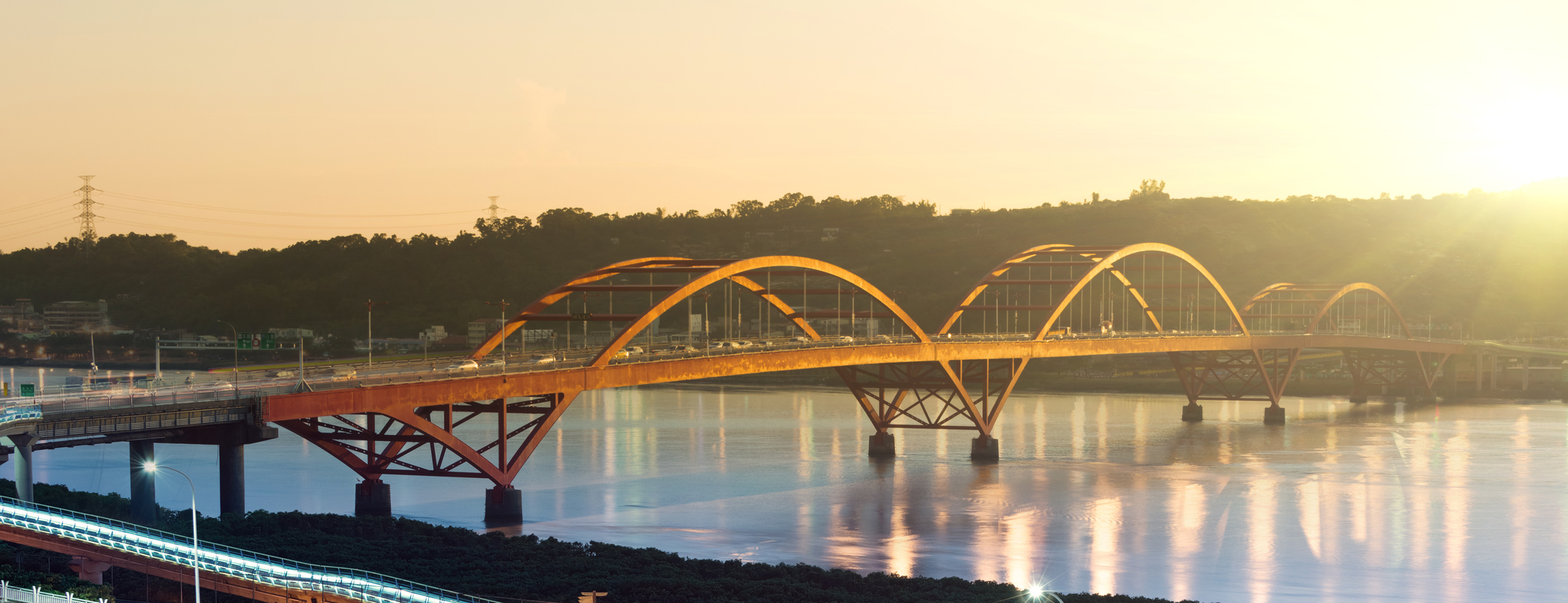 A golden sunset reflects over a bridge with multiple arches spanning across the 
