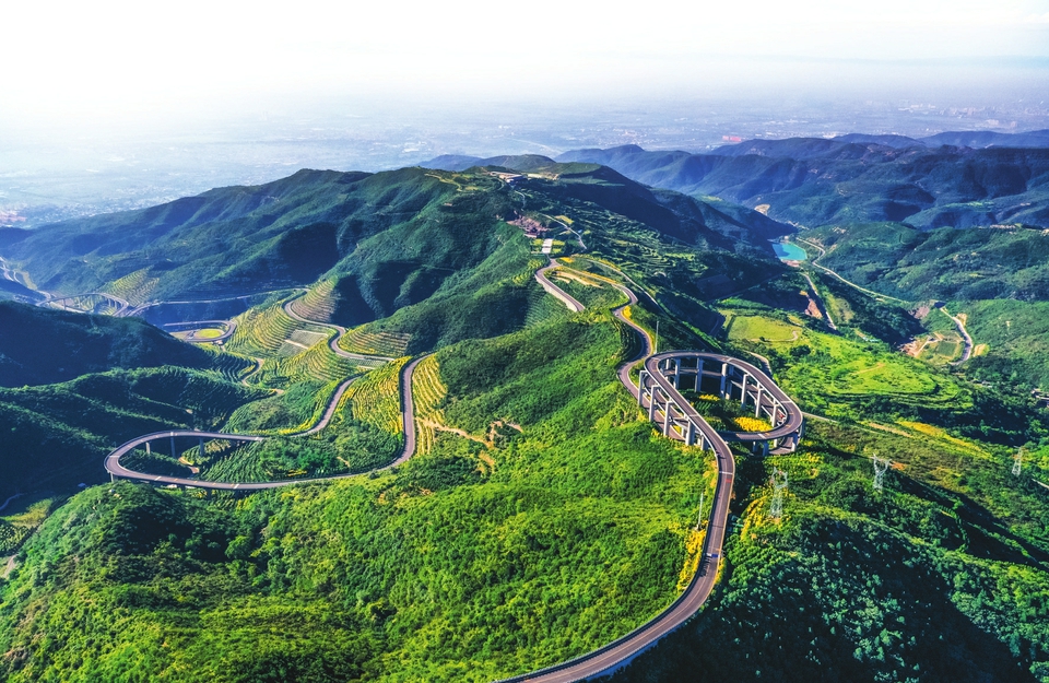 西山国家矿山公园生态修复后的山坡，蜿蜒的道路穿过重新变绿的山体。