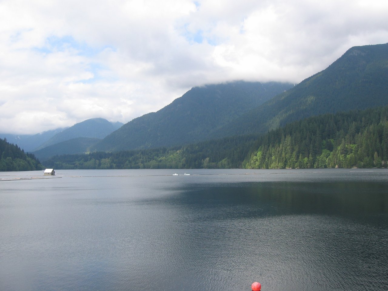 从坝顶朝北看 Capilano Reservoir 水面，平静水面背后是封闭集水区山谷和不可进入的岸线