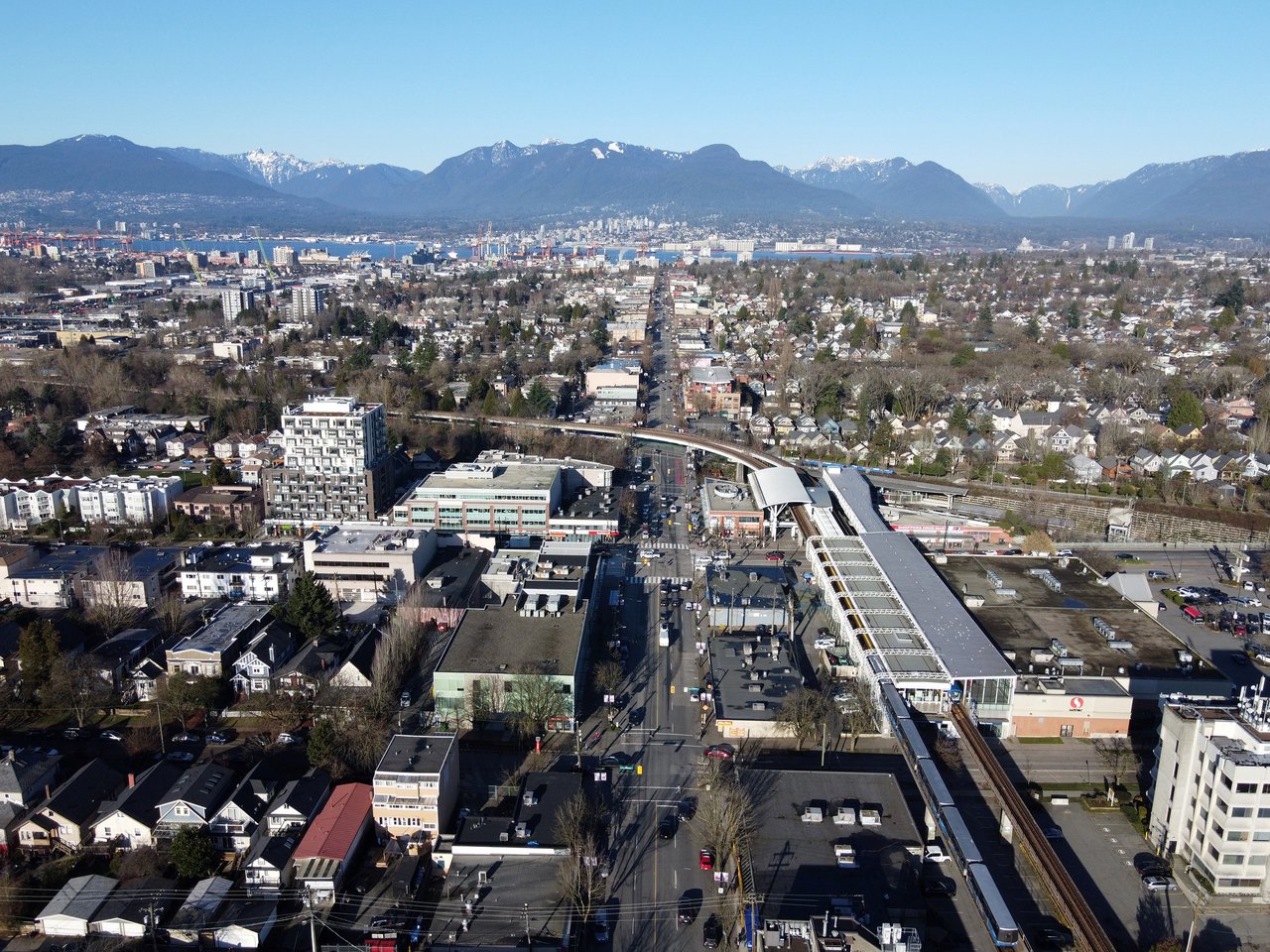 2026 年从 Commercial Drive 向北看的连续街面，小开间店铺、餐饮招牌和远处山体同时出现在街道视野里