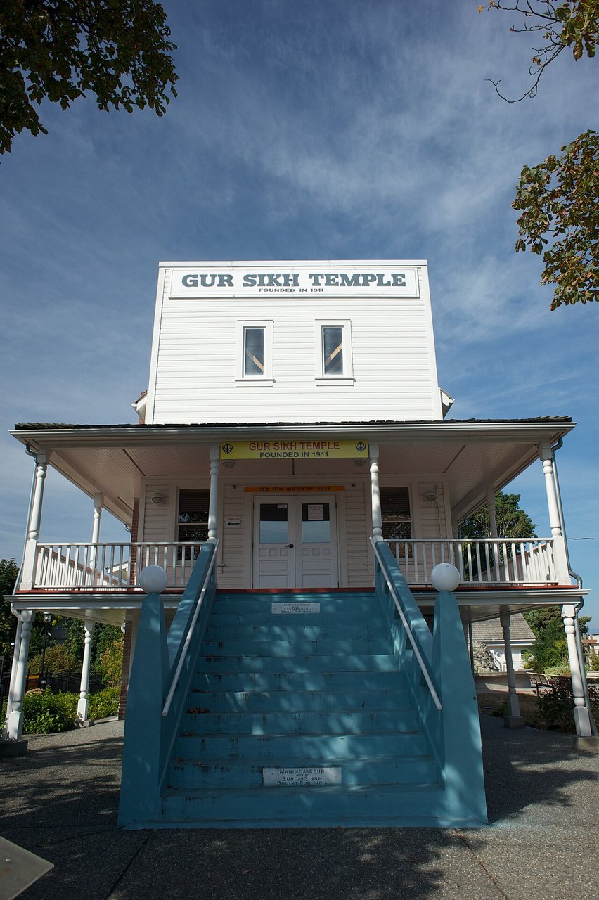 Gur Sikh Temple 侧面视角，可见二楼 veranda 的柱子和围栏、实际山墙屋顶的三角轮廓、木 siding 拼接细节