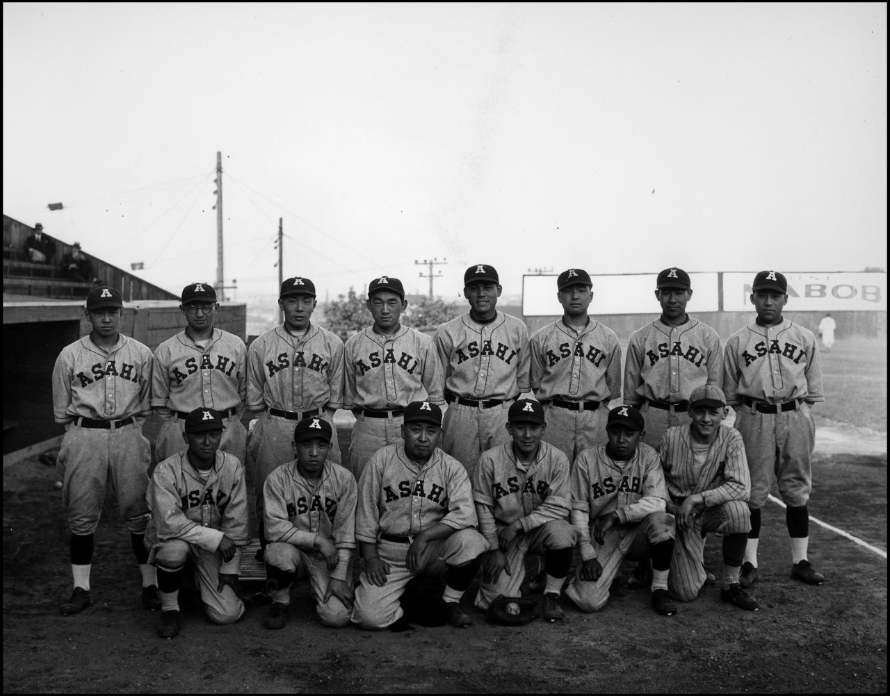 1929 年 Asahi 棒球队合影，球员穿着棒球服在 Oppenheimer Park(当时称 Powell Street Grounds)前拍摄