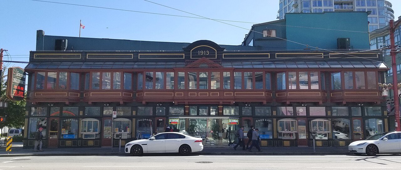 Sam Kee Building 正面立面，二楼连续凸窗压在一层窄店面上方，Jack Chow Insurance 霓虹招牌覆盖街角