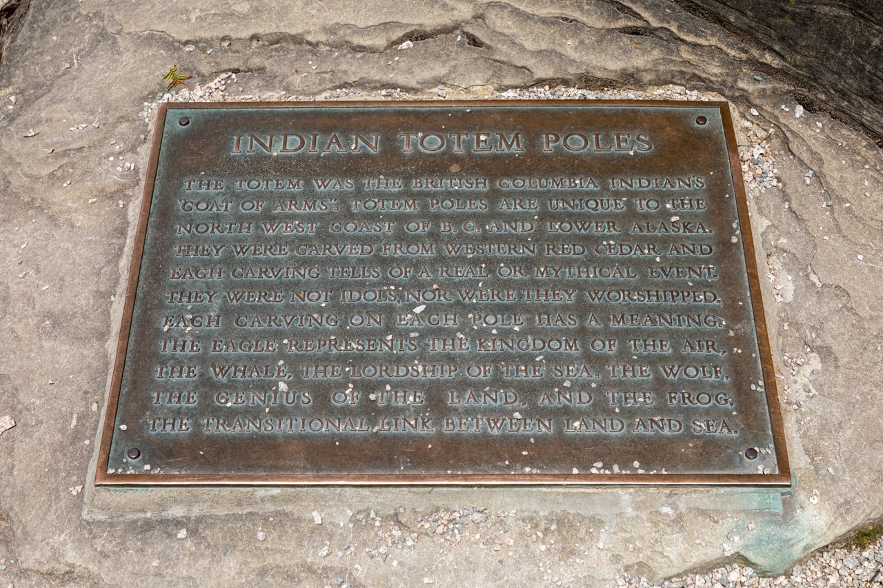 Brockton Point 九根 totem pole 柱群，底座铭文标注来源民族和替代年代
