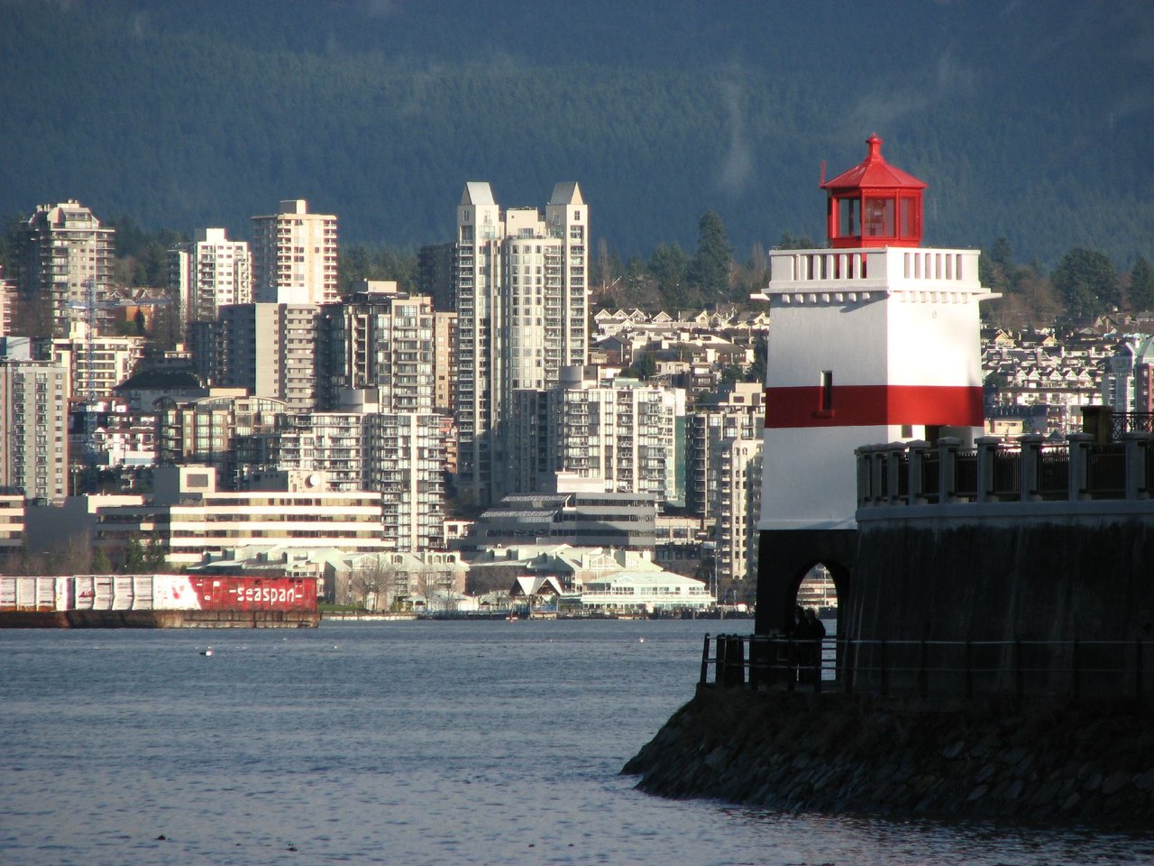 Brockton Point Lighthouse 白色方形塔身配红色横带，底部拱形通道下方是 Seawall 步道，Cunningham 1914 年主持建造