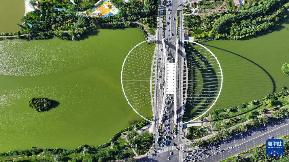 A bridge with a distinctive circular support structure spans over a river, with 