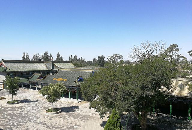 A traditional Hui village with green-tiled roofs and trees lining a paved courty