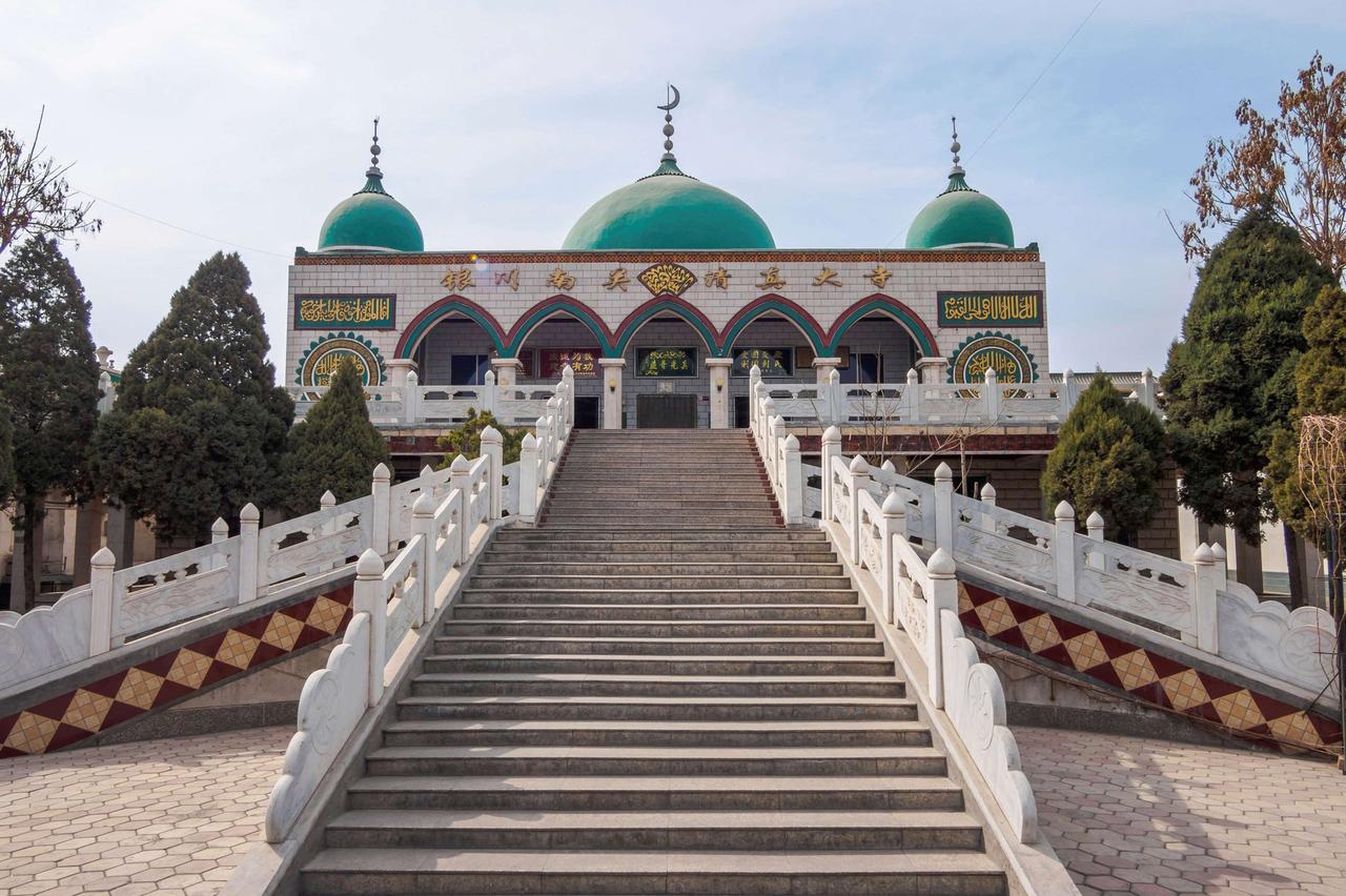 三座歇山顶的清真寺建筑在树木之间,前有一段阶梯通向门口,门楼装饰有阿拉伯文字和图案。